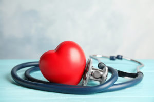 A stethoscope wrapped around a red heart on a wooden table.